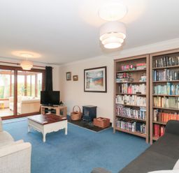 A living room with bookshelves a coffee table sofas and a television near large glass doors leading to a sunroom at Morgan House in Middlezoy