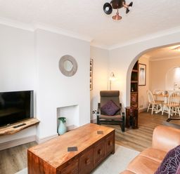 A living room with a wooden coffee table television on a wall shelf and an archway leading to a dining area at 57 Southend Road in Hunstanton