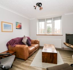 A living room with a brown leather sofa a wooden coffee table and a wall-mounted television at 57 Southend Road in Hunstanton
