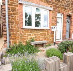 A front garden with plants wooden fence bench and a house with a white door and brick wall at 57 Southend Road Hunstanton