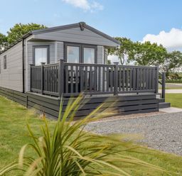 A small grey mobile home with a porch and railing on grass at Happy Daze in Carnaby near Bridlington