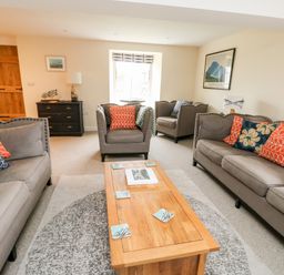 A living room with gray sofas and armchairs around a wooden coffee table at 8 Llwyn Onn in Llanfairpwllgwyngyll