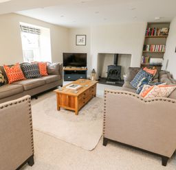 A living room with two beige sofas a wooden coffee table a wood burning stove and a bookshelf at 8 Llwyn Onn in Llanfairpwllgwyngyll