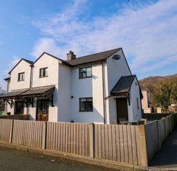 A two-story white house with a wooden fence and a small patio with chairs at Aran in Beddgelert