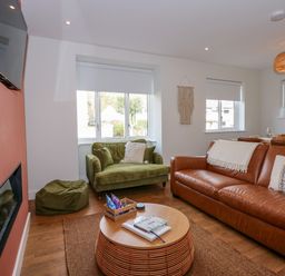 A living room with a brown leather sofa green armchair and beanbag near windows with white blinds and a mounted television at Aran in Beddgelert