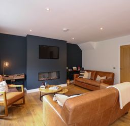 A living room with brown leather sofas a wooden rocking chair a mounted television and a modern fireplace at Craig y Llan in Beddgelert