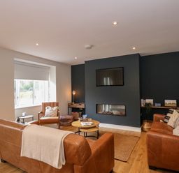 A living room with brown leather sofas a chair a wall-mounted TV and a built-in fireplace at Craig y Llan in Beddgelert