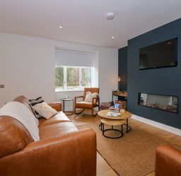A living room with brown leather sofas a chair a nested coffee table a wall-mounted TV and a fireplace at Craig y Llan in Beddgelert