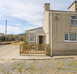 The exterior of a house with a small fenced patio area and surrounding gravel and grass at Cwm Ceiliog Annex in Llanaelhaearn near Trefor