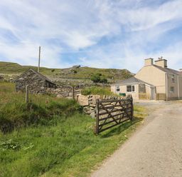 A driveway with a wooden gate leading to a house and a small stone building in rural landscape at Cwm Ceiliog Annex in Llanaelhaearn near Trefor