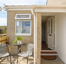 A small outdoor seating area with two chairs and a table next to an open door at Cwm Ceiliog Annex in Llanaelhaearn near Trefor