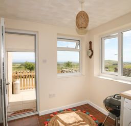 A utility room with a round rug a charcoal grill a washing machine and windows overlooking a rural landscape at Cwm Ceiliog Annex Llanaelhaearn near Trefor