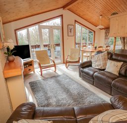 A living room with leather sofas two chairs a dining table and large windows at 4 The Oaks in Swarland