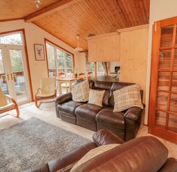 A living room with leather sofas and armchairs next to a dining table and glass doors at 4 The Oaks in Swarland