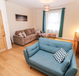 A living room with two sofas a wooden door a small table a television on a wooden cabinet and curtains at Ty Cwtch in Tenby