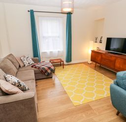 A living room with a brown sofa blue armchair yellow rug and wooden TV console at Ty Cwtch in Tenby