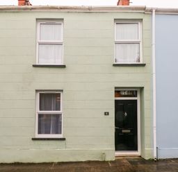 A pale green house facade with three windows and a black front door numbered 6 at Ty Cwtch in Tenby