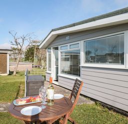 An outdoor patio area with a wooden table and chair set with wine glasses a bottle of wine and a platter of snacks next to a grey building at Wagtails Norton near Dartmouth