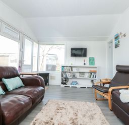 A living room with brown leather sofa and chair a bookshelf and TV at Wagtails in Norton near Dartmouth