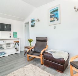 A sitting area with two armchairs a footstool bookshelf with books and a television on the wall at Wagtails in Norton near Dartmouth