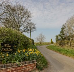 A country road with daffodils and a sign that says The Stables at The Stables in Belbroughton