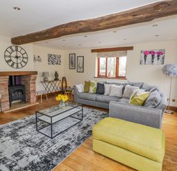 A living room with a grey sofa a yellow ottoman a brick fireplace and large wall clock at The Stables in Belbroughton