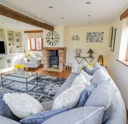 A living room with a gray sofa and cushions a glass coffee table a fireplace and a television at The Stables in Belbroughton