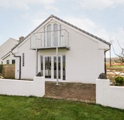 A white house with a glass balcony and patio doors facing a grassy yard at The Annex in Ulverston