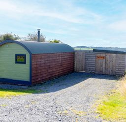 A small wooden cabin with a curved roof and a shed with a sign reading Dew Pond in a rural area at Dew Pond in Blagdon
