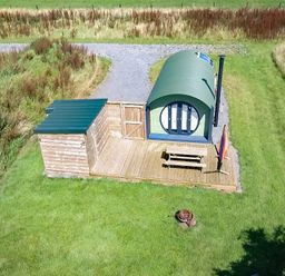 A small green curved cabin with a wooden deck picnic table and umbrella on grass at Dew Pond in Blagdon
