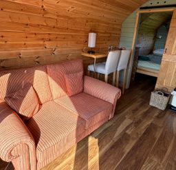 A wooden interior room with a striped sofa two chairs at a small table and a view into a bedroom at Dew Pond in Blagdon