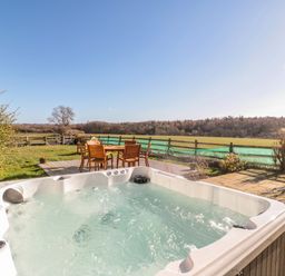 An outdoor hot tub and wooden table with chairs on a deck overlooking fields at Thistleyhaugh Cottage in Longhorsley near Longframlington