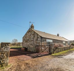 A stone cottage with a wooden gate and surrounding wall on a dirt road at Thistleyhaugh Cottage in Longhorsley near Longframlington