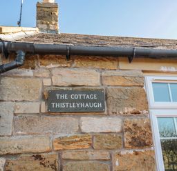 Stone exterior wall with a sign reading The Cottage Thistleyhaugh next to a white window at Thistleyhaugh Cottage in Longhorsley near Longframlington