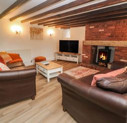 A living room with leather sofas a coffee table a television and a fireplace at Trevedran Cottage in St Buryan