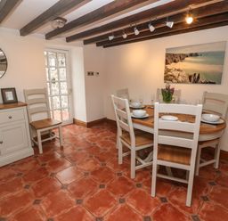 A dining room with a wooden table set for six chairs and a buffet with fruit at Trevedran Cottage in St Buryan