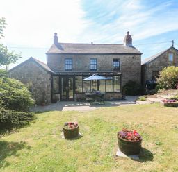A stone cottage with a patio table and umbrella in a garden with two flower pots at Trevedran Cottage in St Buryan