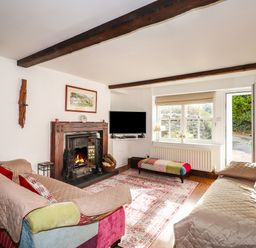 A living room with two sofas a fireplace a television a window and an open door at Bay Tree Cottage in Ambleside
