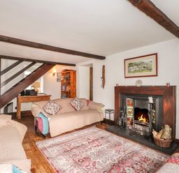 A living room with sofas a fireplace wooden beams a rug and a television at Bay Tree Cottage in Ambleside