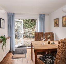 A dining area with a wooden table and woven chairs next to open glass doors leading to a stone patio at Bay Tree Cottage Ambleside