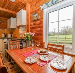 A kitchen and dining area with a wooden table set for three and a window overlooking a field at Orchard Lodge in Hockworthy near Sampford Peverell Devon