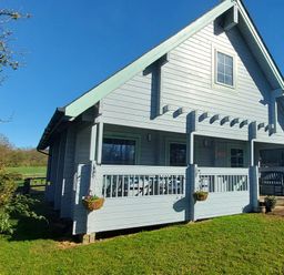 A wooden house with a porch and hanging baskets on grass at Orchard Lodge in Hockworthy near Sampford Peverell Devon