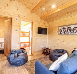 A wooden living room with blue sofa bean bags wall mounted tv and framed cow picture at Clover Lodge in Theberton near Leiston