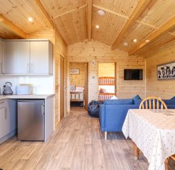 An open wooden interior with a kitchen area on the left a dining table with chairs on the right and a blue sofa in the center at Clover Lodge Theberton near Leiston