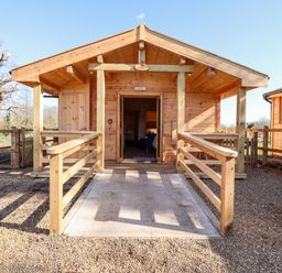 A wooden cabin with a ramp and railing outside surrounded by gravel at Clover Lodge Theberton near Leiston