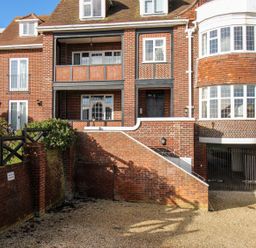 The exterior of a multi-story brick building with balconies, bay windows, steps leading to a door, and a gated driveway at Ocean Watch 5 in Greenhill