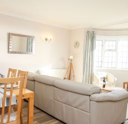 A living room and dining area with wooden chairs a beige sofa and bay windows at Ocean Watch 5 in Greenhill