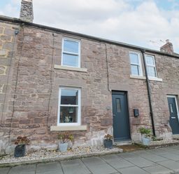A stone facade house with two windows a dark door and potted plants on a sidewalk at Castle Keep in Norham