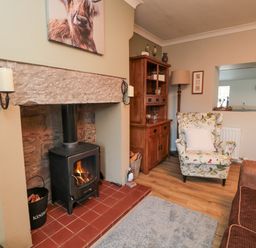 A living room with a wood stove fireplace floral armchair wooden cabinet and brown sofa at Castle Keep in Norham