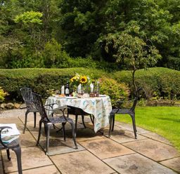 A garden patio with a table set for dining surrounded by chairs and green hedges at The Old Post House at Low Stott Park in Low Stott Park near Newby Bridge